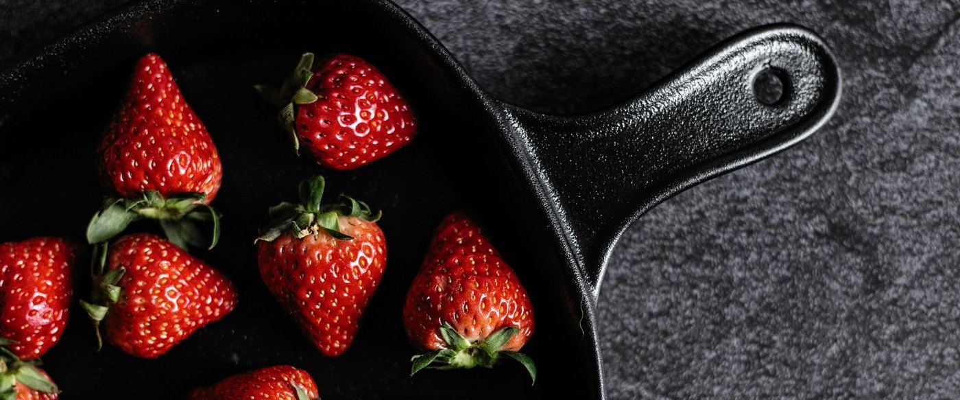Fresh strawberries in a cast-iron skillet beside a bowl of cherries